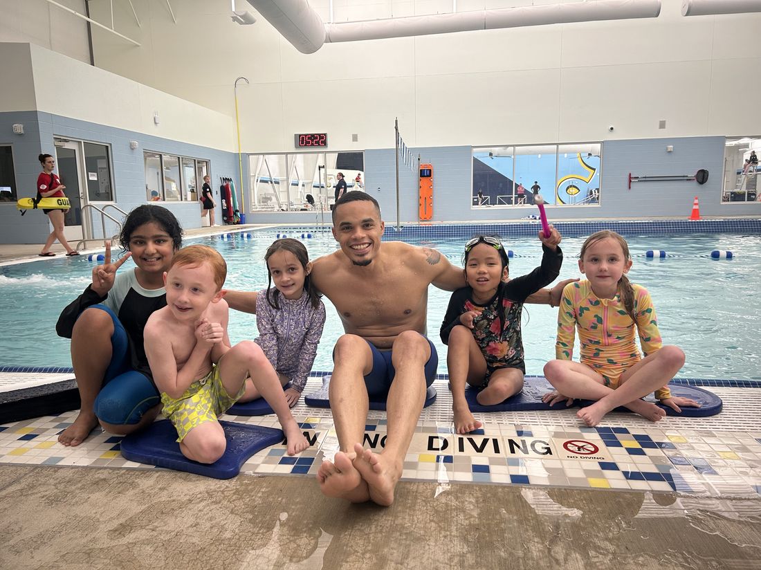 Coach Alexander poolside with a group of young swim students