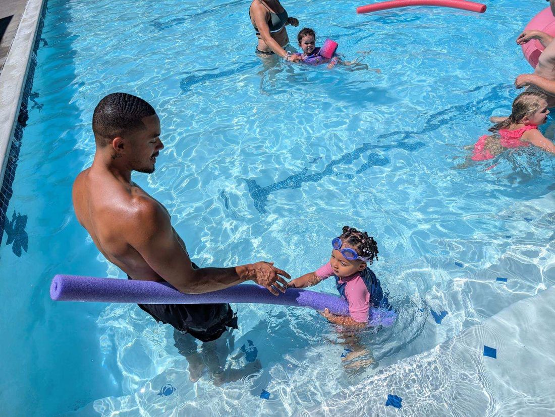 Coach Alexander guiding a toddler with a pool noodle